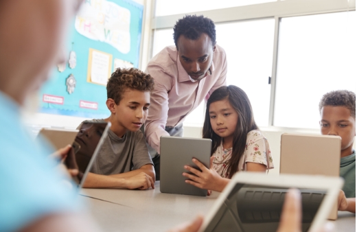 A teacher helping two students on a tablet.