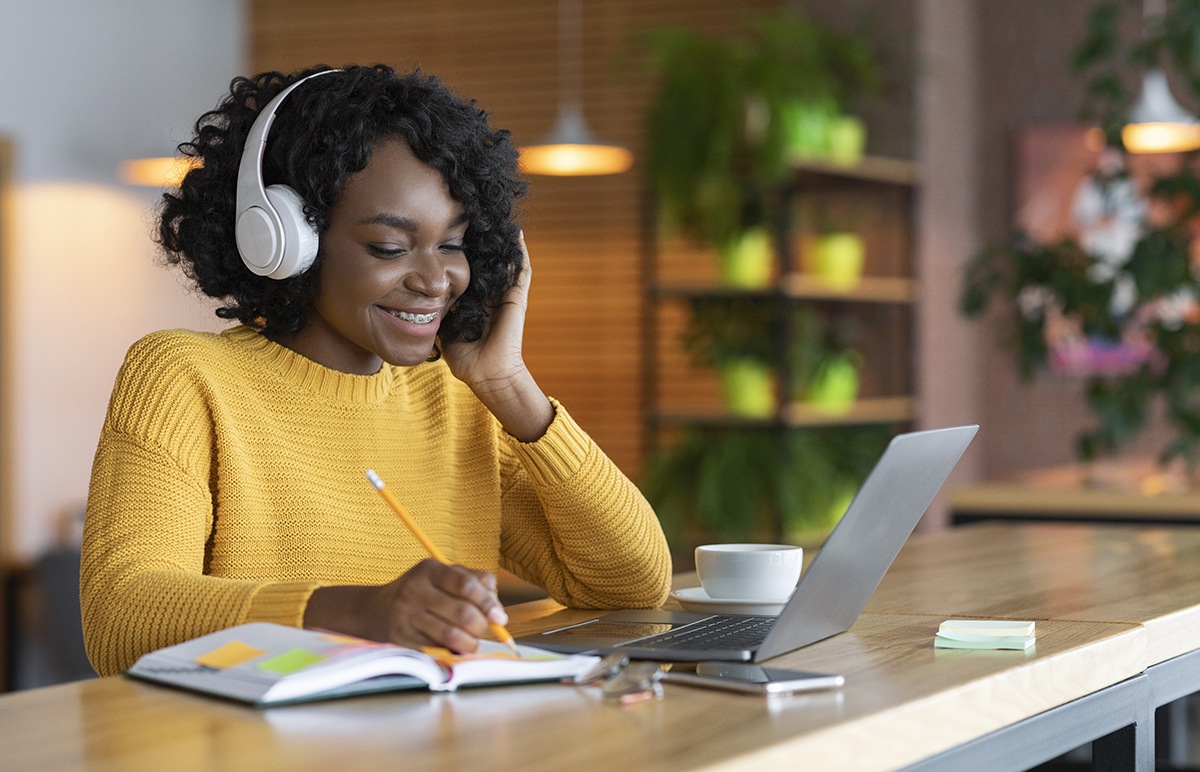 Happy student on laptop listening on headphones