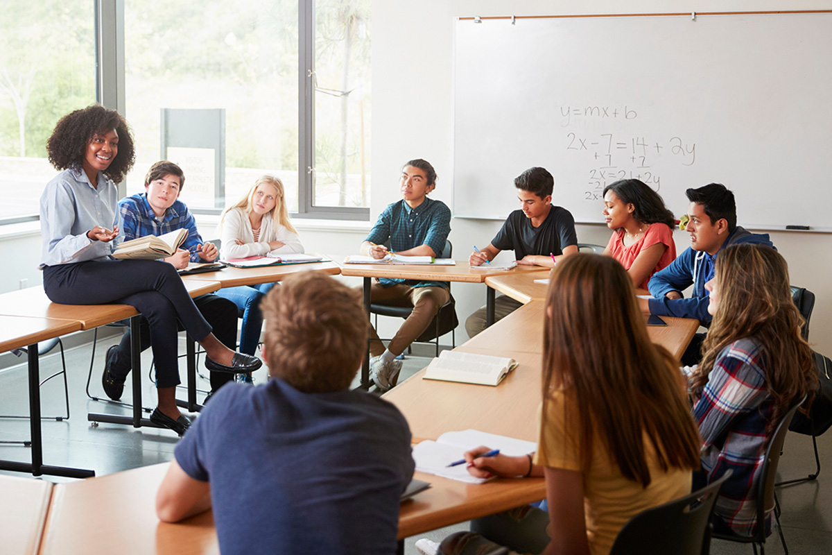 a group of students sitting around a table listening to the teacher