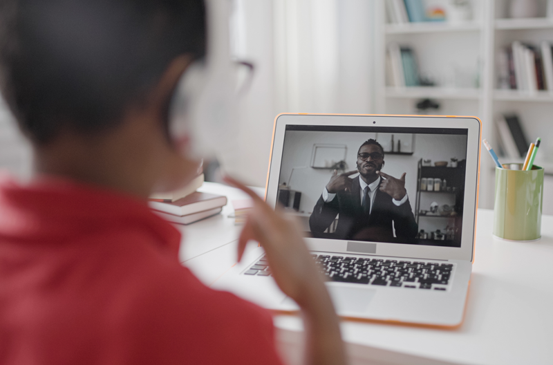 Elementary student wearing headphones and watching instructor on laptop