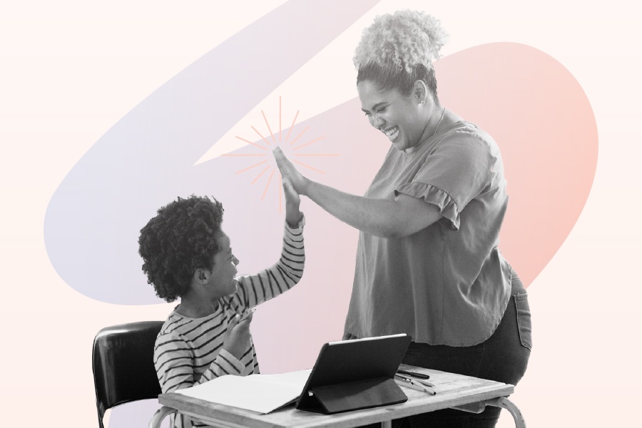 Elementary student sitting at desk with a laptop and high-fiving their teacher