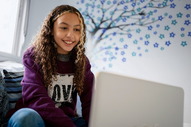 Middle school student sitting and typing on laptop.