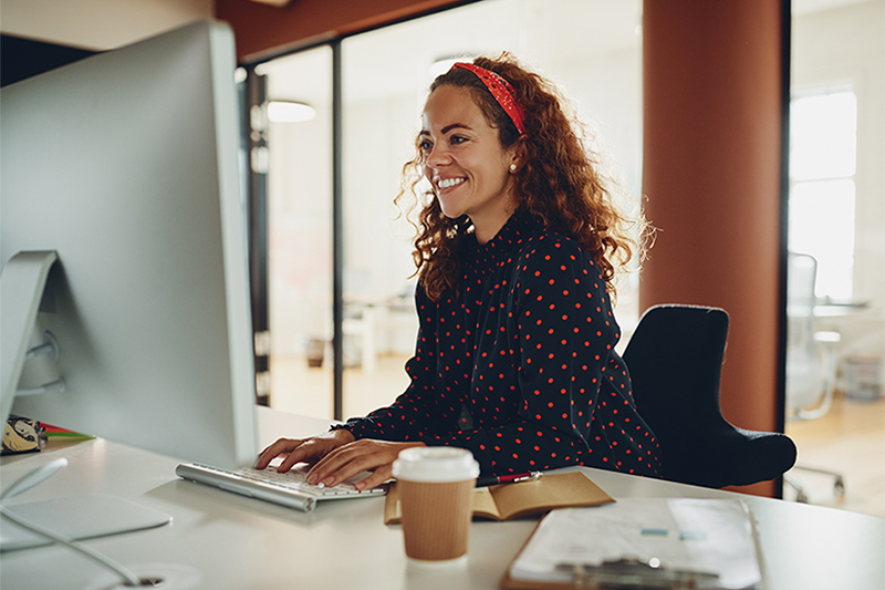 Educator sitting at a desk while typing on a keyboard and smiling at a monitor