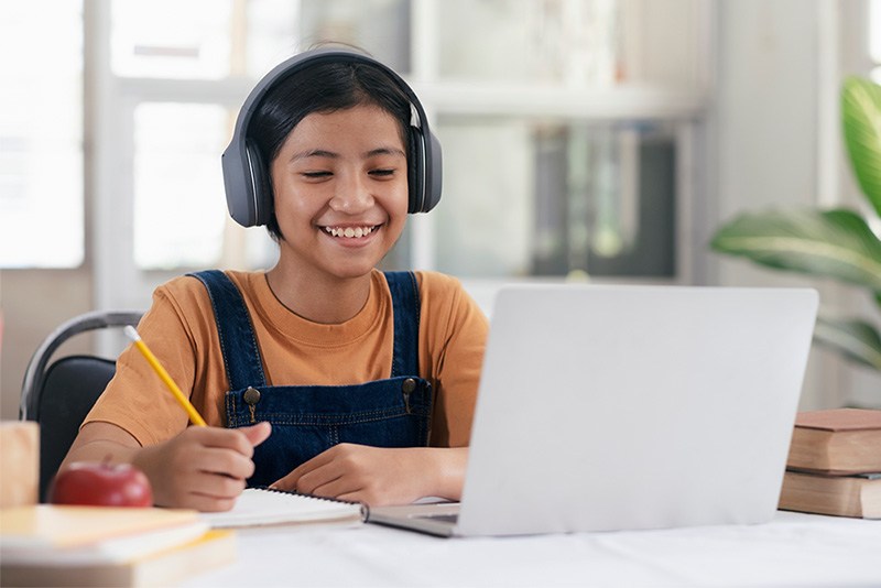 Middle school student wearing headphones and smiling at their tutor on a laptop.