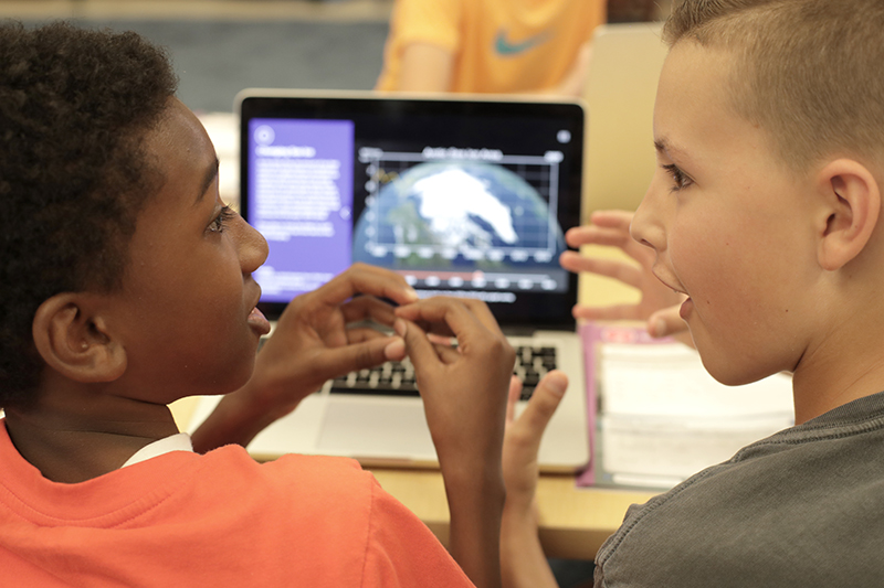 Two students interacting with each other while engaged in a Twig Science lesson on a laptop