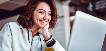 High school student looking at laptop while smiling and resting hand on chin