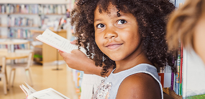 Elementary student smiling and holding an open book in a school library