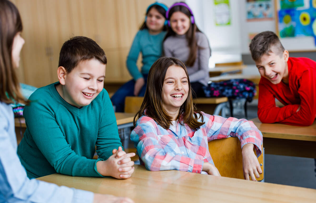 A young girl seated at a classroom table laughing with other students