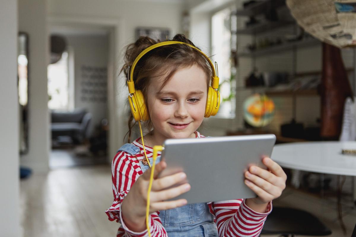 A young girl wearing headphones using a tablet in her hands