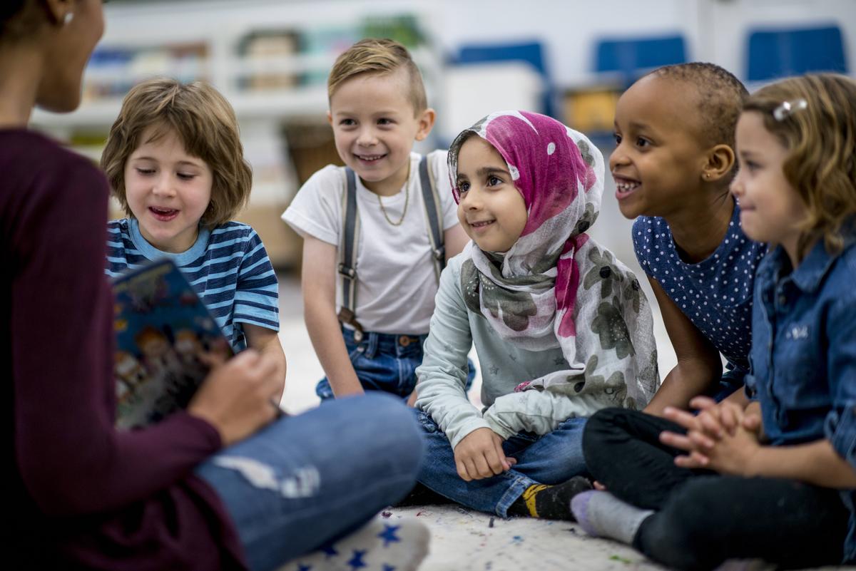 A young girl in hijab sitting in a group of students listening to a teacher speak