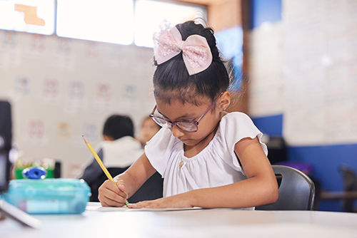 An elementary-aged student in a classroom is focused on writing, using the Imagine Learning EL Education program.