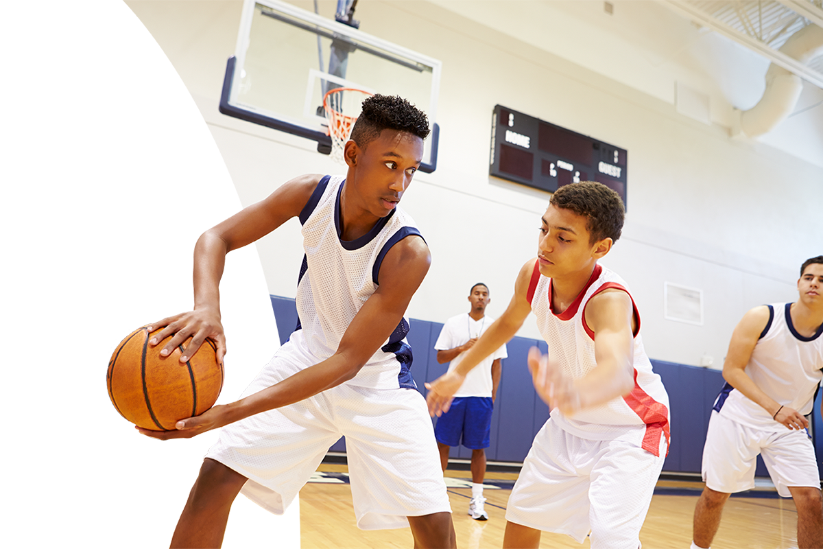 Opposing high school basketball players holding and guarding a basketball on an indoor court